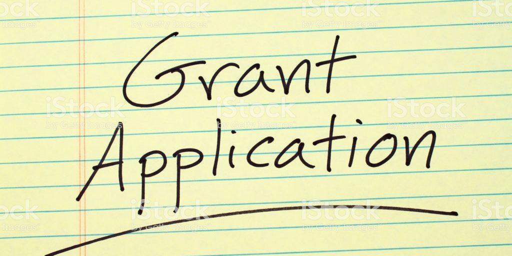 The word “Grant Application” underlined on a yellow legal pad